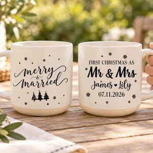 May include: Two off-white ceramic mugs with black text and snowflake graphics. One mug reads merry & married with three pine trees. The other reads FIRST CHRISTMAS AS Mr & Mrs James ♥ Lily 07.11.2026 with scattered snowflake accents.