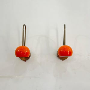 May include: Two wall-mounted lamps with orange, spherical shades. The lamps have a brass-colored, curved arm and a circular base. The lamps are mounted on a white wall, providing a clean and modern aesthetic. The lamps are a decorative lighting fixture.