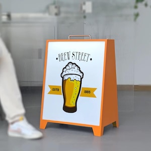 以下が含まれることがあります： ビールグラスのグラフィックと「BREW STREET」の文字が描かれた白いパネルが付いた、オレンジ色のA型看板。看板には、黄色のバナーに「ESTB 1985」の文字も含まれています。上部には金属製のハンドルが付いています。