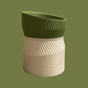 Puede incluir: Un recipiente decorativo de dos tonos con una superficie texturizada. La sección superior es verde oliva y la sección inferior es blanquecina. El diseño presenta líneas diagonales, creando un efecto acanalado. El recipiente tiene una abertura única e inclinada.