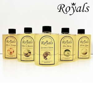 May include: Five amber glass bottles with black lids and labels. Each bottle contains reed diffuser oil and has a different scent: Sweet Orange, Mint & Jasmine, Lavender & Vanilla, Sea Spray, and Fresh Linen. The bottles are arranged in a row on a white surface. The label on each bottle reads "Royals" and includes the scent name and "Quality Fragrances Made in UK."