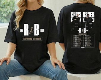 May include: Black t-shirt featuring "The R&B Tour" with "Raymond & Brown" text. The back of the shirt displays "Chris Usher" and "R&B" tour dates. The shirt is a classic crew neck style.