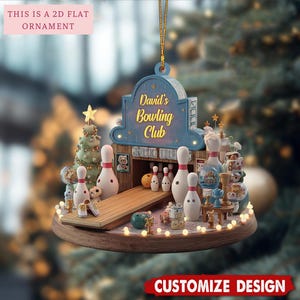 May include: A 2D flat ornament featuring a bowling alley scene with a blue sign reading David's Bowling Club. The design includes white bowling pins, a wooden lane, a yellow ball, a green tree, and small decorative figures on a round base.