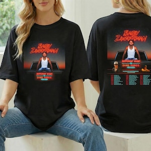 May include: Black t-shirt featuring a graphic of Bailey Zimmerman on the front and back. The front graphic shows Zimmerman sitting on a truck bed with the text "Different Night Same Rodeo." The back graphic includes tour dates.