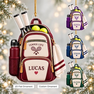 Puede incluir: Un adorno plano de acrílico con forma de mochila que incluye dos raquetas de tenis, dos pelotas amarillas, una botella de agua y una toalla. La bolsa muestra el texto TENNIS LIFE, un icono de raqueta y un nombre en colores granate y crema.