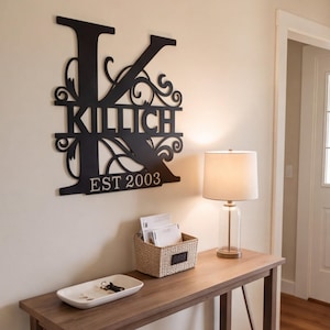 Pode incluir: Um grande letreiro de parede em forma de letra K preta com o nome KILLICH em letras maiúsculas no centro e o texto EST 2003 na parte inferior. O design inclui ornamentos decorativos integrados na estrutura da letra.