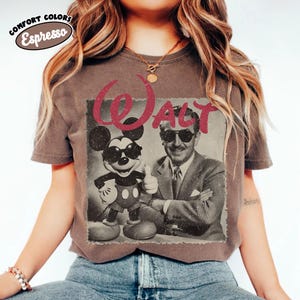 K&ouml;nnte beinhalten: Ein braunes T-Shirt mit einem Retro-Grafik von Mickey Mouse und Walt Disney, beide mit Sonnenbrille. Das Wort "WALT" ist rot &uuml;ber dem Bild gedruckt. Das Shirt hat die Worte "COMFORT COLORS Espresso" oben links aufgedruckt.