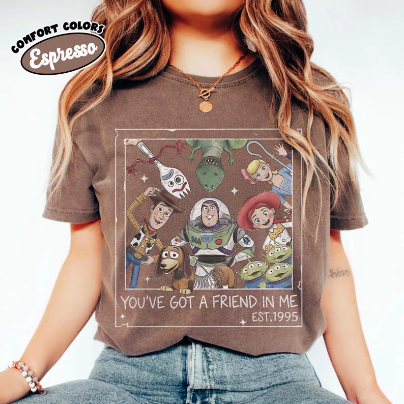 May include: Espresso-colored t-shirt featuring a graphic of characters from the animated film "Toy Story." The design includes Woody, Buzz Lightyear, and other characters, with the text "YOU'VE GOT A FRIEND IN ME EST.1995."