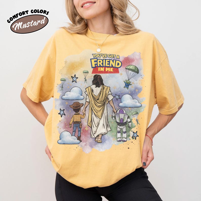 May include: Mustard-colored t-shirt with the text "YOU'VE GOT A FRIEND IN ME" and a graphic of Jesus walking with a child and cartoon characters. The shirt is a Comfort Colors brand.