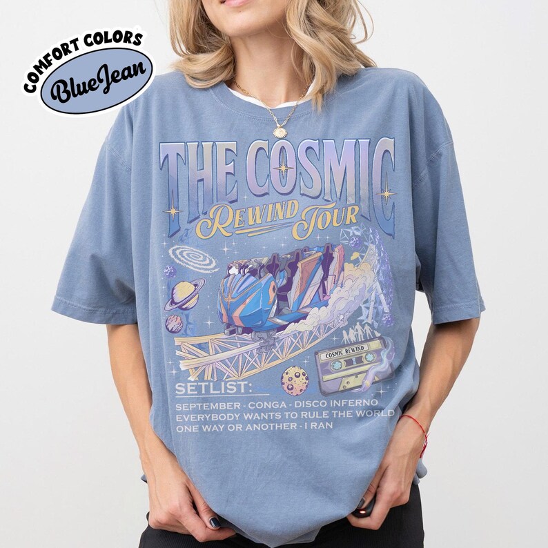 K&ouml;nnte beinhalten: Blaues Comfort Colors T-Shirt mit "THE COSMIC REWIND TOUR" Grafik. Das Design zeigt eine Achterbahn, Planeten und eine Kassette. Die Setlist enth&auml;lt Songs wie "September" und "Everybody Wants to Rule the World".