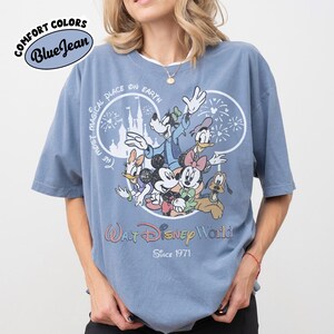 May include: Blue short-sleeved t-shirt with a graphic of Disney characters, including Mickey and Minnie Mouse, Goofy, Donald and Daisy Duck, and Pluto. The shirt has the text "Walt Disney World Since 1971" and "The Most Magical Place on Earth."