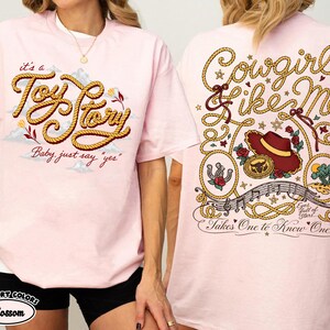 以下が含まれることがあります： ライトピンクのTシャツ。前面にはロープ風の文字で「it's a Toy Story Baby, just say "yes"」とプリントされています。背面には「Cowgirl like Me」と「Takes One to Know One」の文字、帽子、蹄鉄、ロープのグラフィックが描かれています。