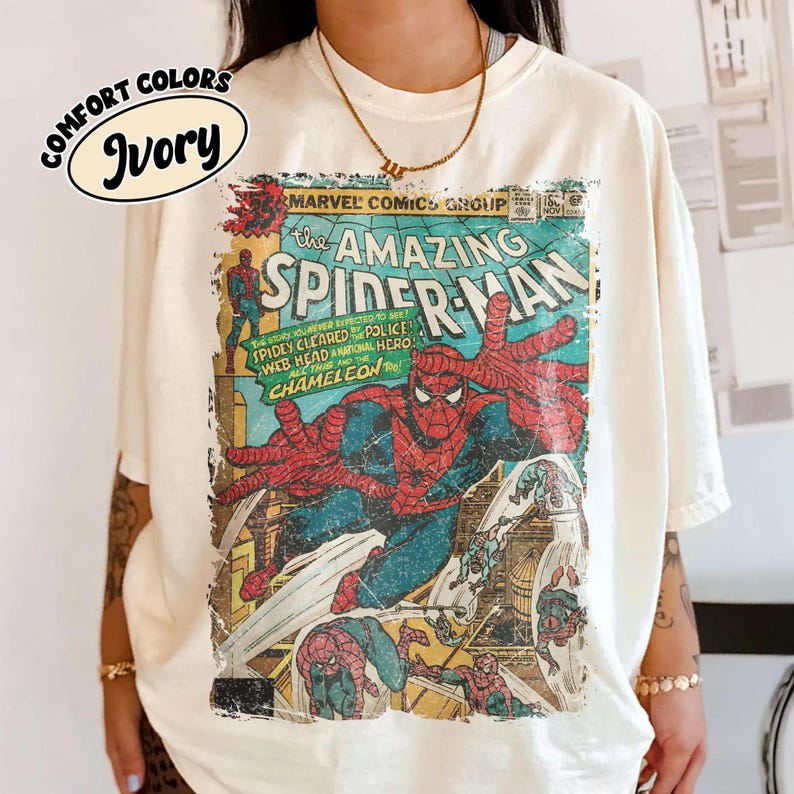 May include: An ivory t-shirt featuring a vintage-style Marvel Comics graphic of The Amazing Spider-Man. The print displays Spider-Man in his red and blue suit, with comic book text including 'The Amazing Spider-Man' and 'Chameleon' in a distressed, weathered aesthetic.