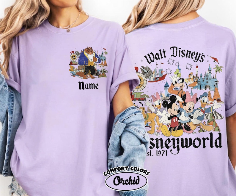 May include: A lilac Comfort Colors t-shirt featuring a Beauty and the Beast graphic on the front and a Disney World design on the back. The front has a Beauty and the Beast graphic with the word "Name" below. The back has Disney characters and the text "Walt Disney's Disneyworld est. 1971".
