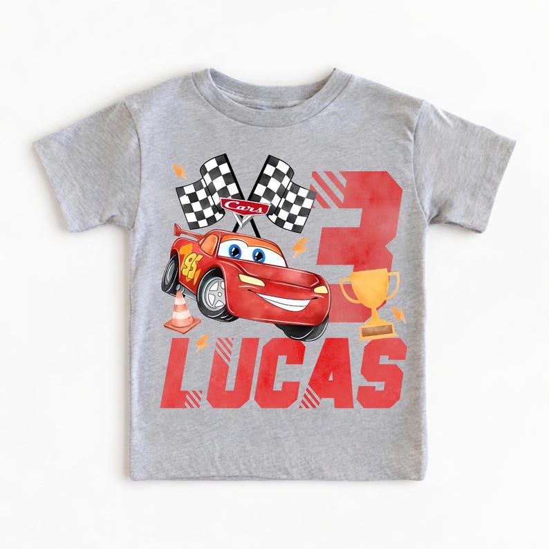 Puede incluir: Camiseta gris con un dise&ntilde;o de coche de carreras rojo, el n&uacute;mero 95, banderas a cuadros y un trofeo dorado. Tambi&eacute;n incluye el n&uacute;mero 3 y el nombre "LUCAS" en rojo. Un dise&ntilde;o divertido para el cumplea&ntilde;os de un ni&ntilde;o.
