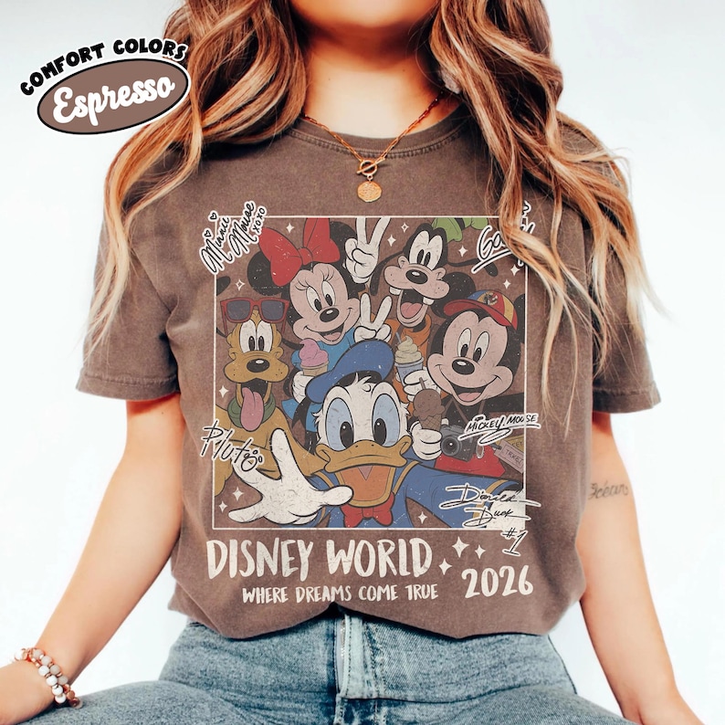 May include: Espresso-colored t-shirt featuring a vintage-style Disney World graphic. The design includes Mickey Mouse, Minnie Mouse, Donald Duck, Pluto, and Goofy. The text "DISNEY WORLD 2026" is prominently displayed, with additional text elements.