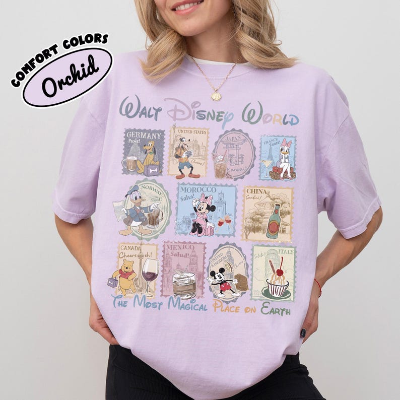 May include: A light purple t-shirt with a Walt Disney World design. The shirt features various Disney characters and country stamps. The text "COMFORT COLORS Orchid" is printed on the top left.