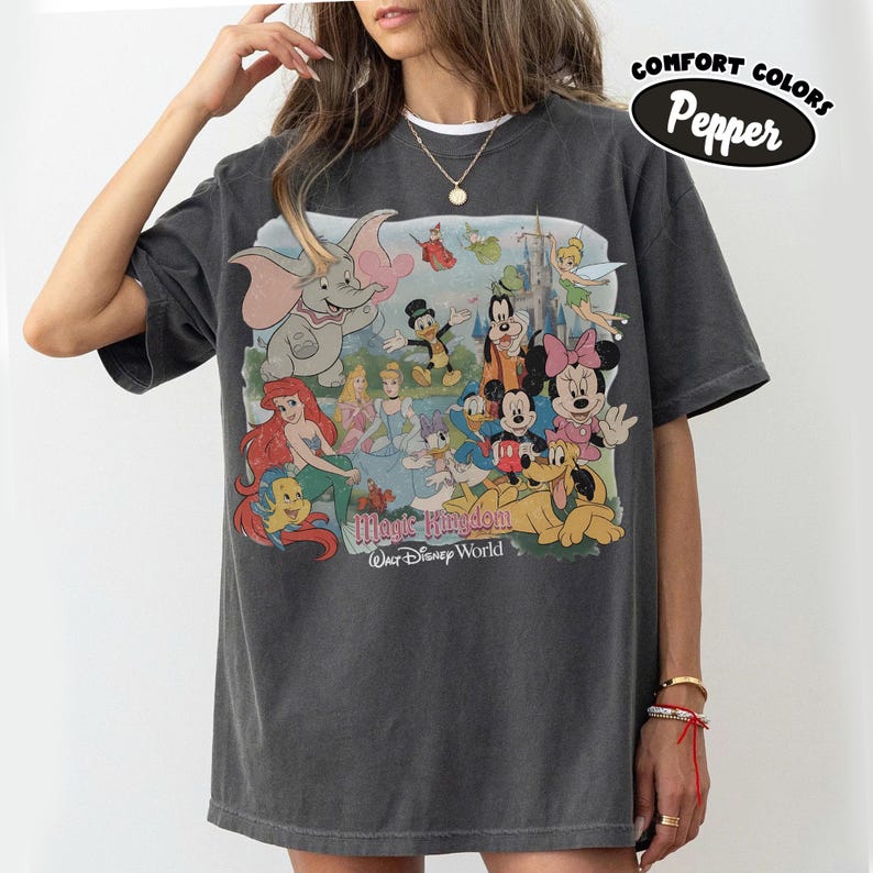 May include: Dark gray t-shirt featuring a colorful graphic of Disney characters, including Dumbo, Ariel, Mickey and Minnie Mouse, and Goofy. The text "Magic Kingdom Walt Disney World" is printed below the characters. The shirt has short sleeves and a crew neck.