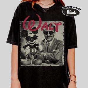 K&ouml;nnte beinhalten: Schwarzes T-Shirt mit einem Vintage-Grafik von Mickey Mouse mit Sonnenbrille und Walt Disney. Das Wort "WALT" in Burgunderrot ist &uuml;ber dem Bild gedruckt. Das Shirt hat einen Used-Look, mit "COMFORT COLORS Black" oben rechts aufgedruckt.