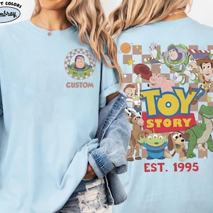Puede incluir: Camiseta azul claro con un gr&aacute;fico de Buzz Lightyear en la parte delantera y un dise&ntilde;o de Toy Story en la parte trasera. El dise&ntilde;o trasero incluye varios personajes, el logotipo de Toy Story y el texto "EST. 1995". La camiseta tiene cuello redondo y mangas cortas.