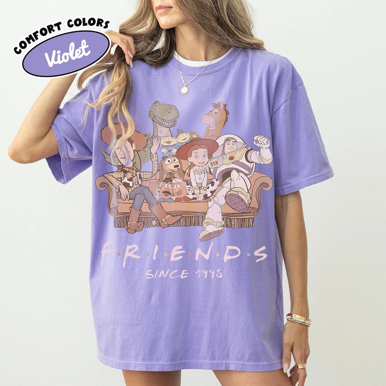 May include: Violet Comfort Colors t-shirt featuring a graphic of Toy Story characters on a brown couch. The word "FRIENDS" is printed in pink, with "SINCE 1995" below. A purple oval with "COMFORT COLORS" and "Violet" is in the upper left.