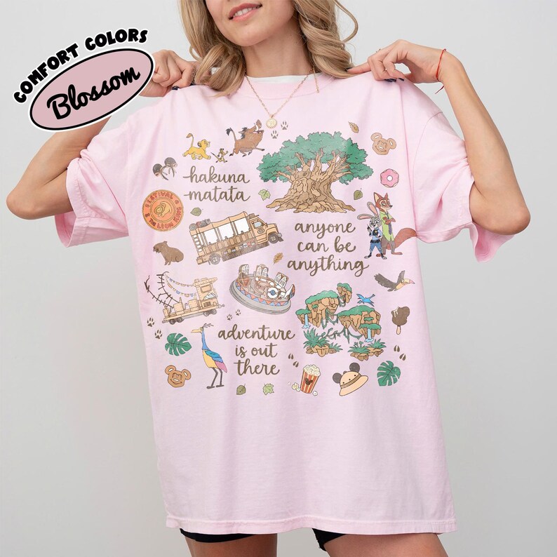 Puede incluir: Camiseta rosa claro con un dise&ntilde;o gr&aacute;fico colorido que presenta personajes de dibujos animados, un &aacute;rbol y las palabras "Hakuna Matata" y "Adventure is out there". La camiseta tambi&eacute;n tiene las palabras "anyone can be anything".