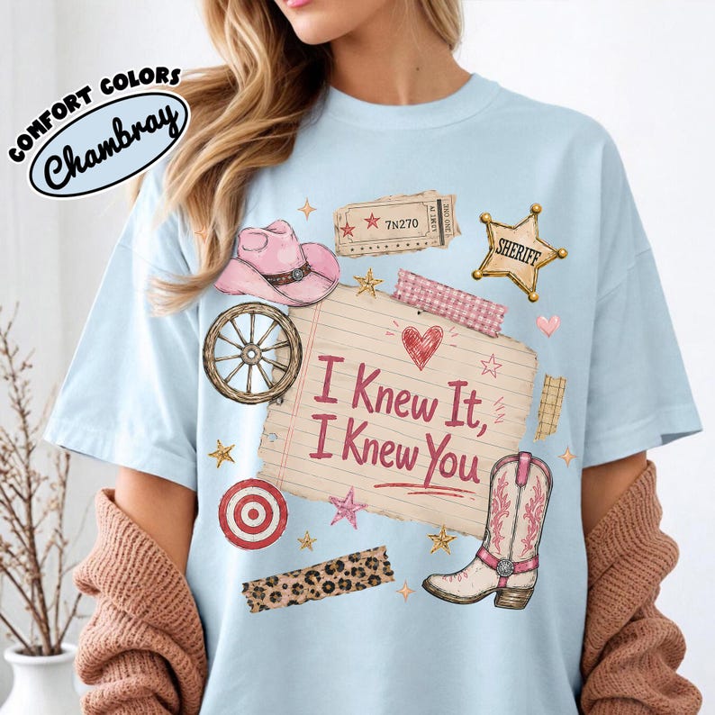 Puede incluir: Una camiseta azul claro con un estampado gr&aacute;fico de un sombrero de vaquero rosa, una rueda de carreta, una estrella de sheriff, una diana, una franja de leopardo y una bota vaquera. El centro muestra el texto I Knew It, I Knew You.