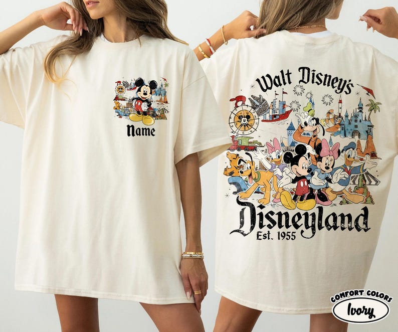 Peut inclure: T-shirt ivoire avec des motifs de Mickey Mouse et Disneyland. L'avant pr&eacute;sente Mickey avec le texte "Name". Le dos affiche des personnages Disney, un ch&acirc;teau et le texte "Walt Disney's Disneyland Est. 1955".