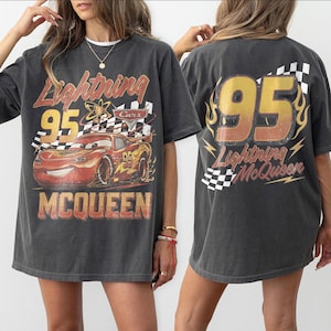 Może przedstawiać: Ciemnoszara koszulka z Lightning McQueen z filmu Auta. Prz&oacute;d przedstawia numer 95, szachownicę i nazwisko McQueen. Tył koszulki r&oacute;wnież przedstawia numer 95 i słowa Lightning McQueen.