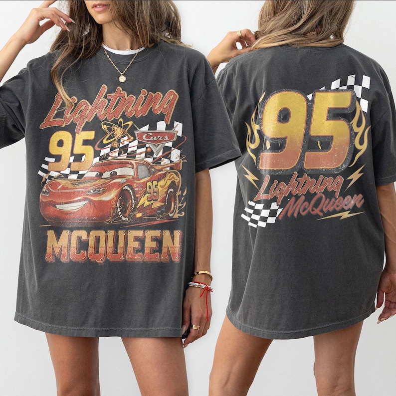 Może przedstawiać: Ciemnoszara koszulka z Lightning McQueen z filmu Auta. Prz&oacute;d przedstawia numer 95, szachownicę i nazwisko McQueen. Tył koszulki r&oacute;wnież przedstawia numer 95 i słowa Lightning McQueen.