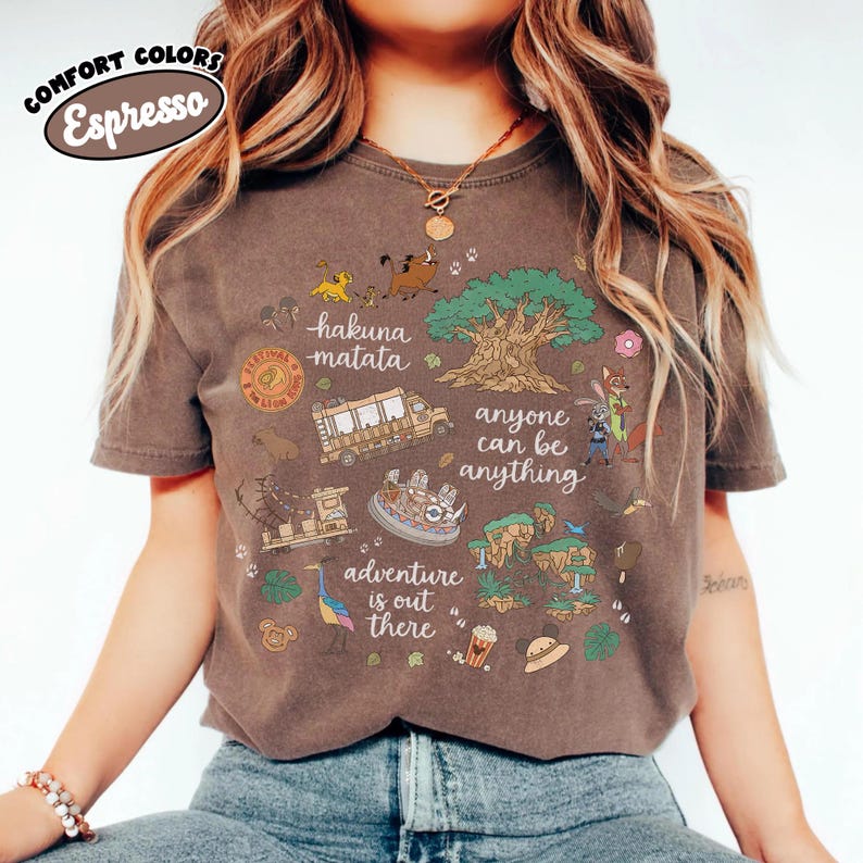 Puede incluir: Camiseta color espresso con un dise&ntilde;o gr&aacute;fico colorido con las palabras "Hakuna Matata", "Anyone Can Be Anything" y "Adventure is Out There". El dise&ntilde;o incluye im&aacute;genes de dibujos animados de animales, un &aacute;rbol y un autob&uacute;s.