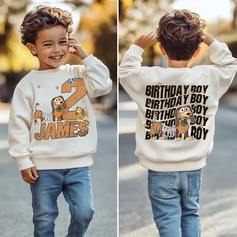 K&ouml;nnte beinhalten: Cremefarbenes Sweatshirt mit einem Cartoon-Hund und der Zahl 2 auf der Vorderseite. Der Name "JAMES" ist unter dem Hund aufgedruckt. Auf der R&uuml;ckseite des Sweatshirts steht mehrfach "BIRTHDAY BOY" mit einem Cartoon-Hund.