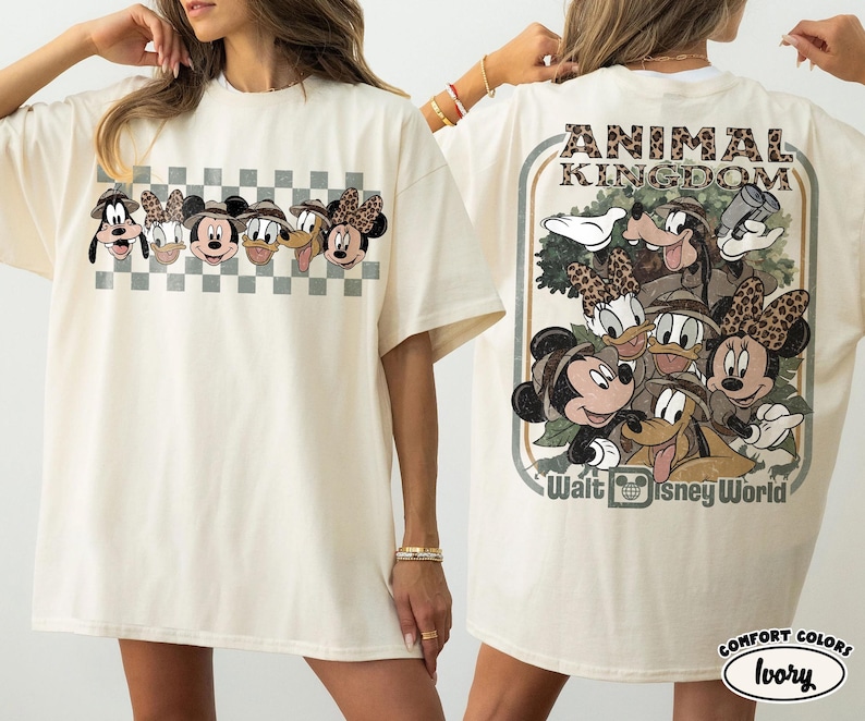 K&ouml;nnte beinhalten: Cremefarbenes T-Shirt mit Disney-Figuren. Auf der Vorderseite sind Gesichter von Figuren auf einem karierten Hintergrund zu sehen. Auf der R&uuml;ckseite befindet sich eine gr&ouml;&szlig;ere Grafik mit den Worten "ANIMAL KINGDOM" und "Walt Disney World".