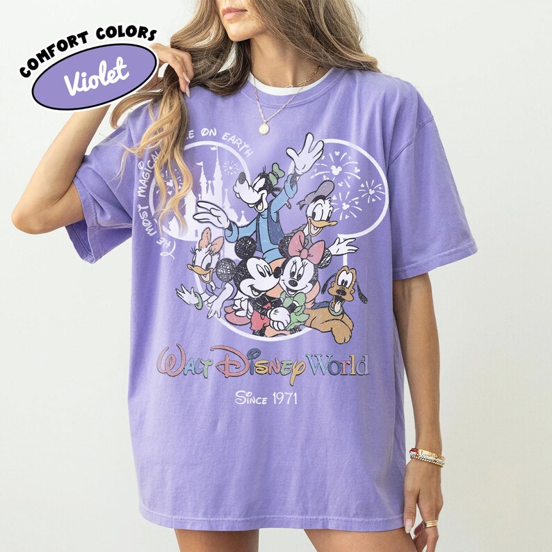 May include: Violet Comfort Colors t-shirt featuring a graphic of Disney characters including Mickey Mouse, Minnie Mouse, Goofy, Donald Duck, and Pluto. The shirt has the text "Walt Disney World Since 1971".
