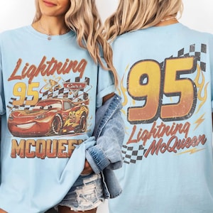 Może przedstawiać: Jasnoniebieska koszulka z Lightning McQueen. Prz&oacute;d przedstawia napis "Lightning 95 McQueen" i wizerunek postaci. Tył prezentuje duży napis "95" i "Lightning McQueen".