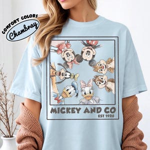 Puede incluir: Camiseta azul claro con una ilustraci&oacute;n enmarcada de Mickey Mouse, Minnie Mouse, Donald Duck, Daisy Duck, Goofy y Chip y Chop. La camiseta tiene el texto "Mickey and Co. Est. 1928" y "Comfort Colors Chambray".