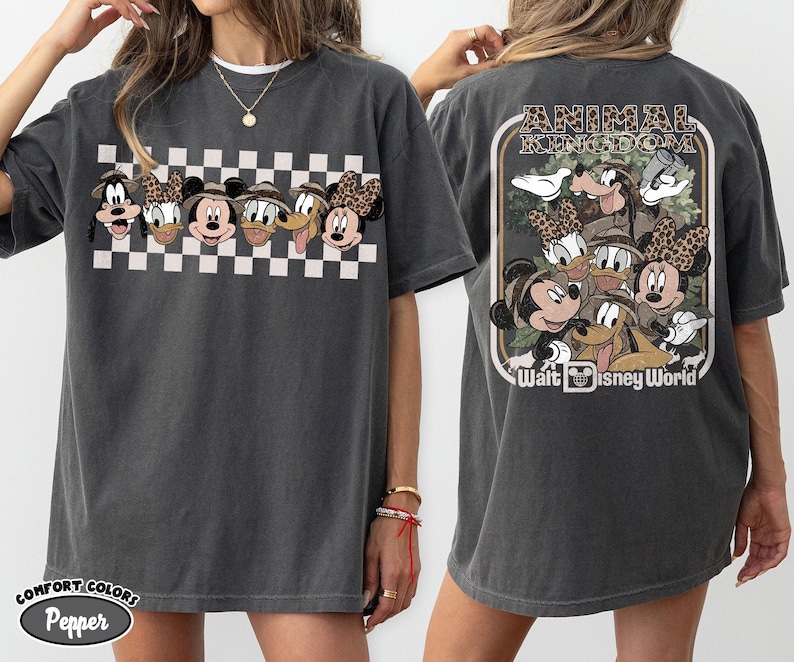 K&ouml;nnte beinhalten: Dunkelgraues T-Shirt mit einem Cartoon-Design von Disney-Figuren, darunter Micky Maus, Minnie Maus, Donald Duck und Goofy. Die Vorderseite hat ein Schachbrettmuster. Auf der R&uuml;ckseite des Shirts steht "Animal Kingdom" und "Walt Disney World".