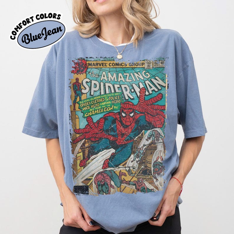 May include: A blue jean colored short-sleeve t-shirt featuring a vintage Marvel Comics The Amazing Spider-Man graphic print on the front. The design displays Spider-Man in a red and blue suit with comic book text and illustrations.