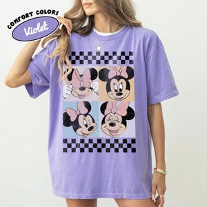 May include: Violet Comfort Colors t-shirt featuring a four-panel design with Minnie Mouse faces. Each panel has a different expression, with a black and white checkered pattern at the top and bottom. The shirt has the text "Comfort Colors" and "Violet" on the top left.