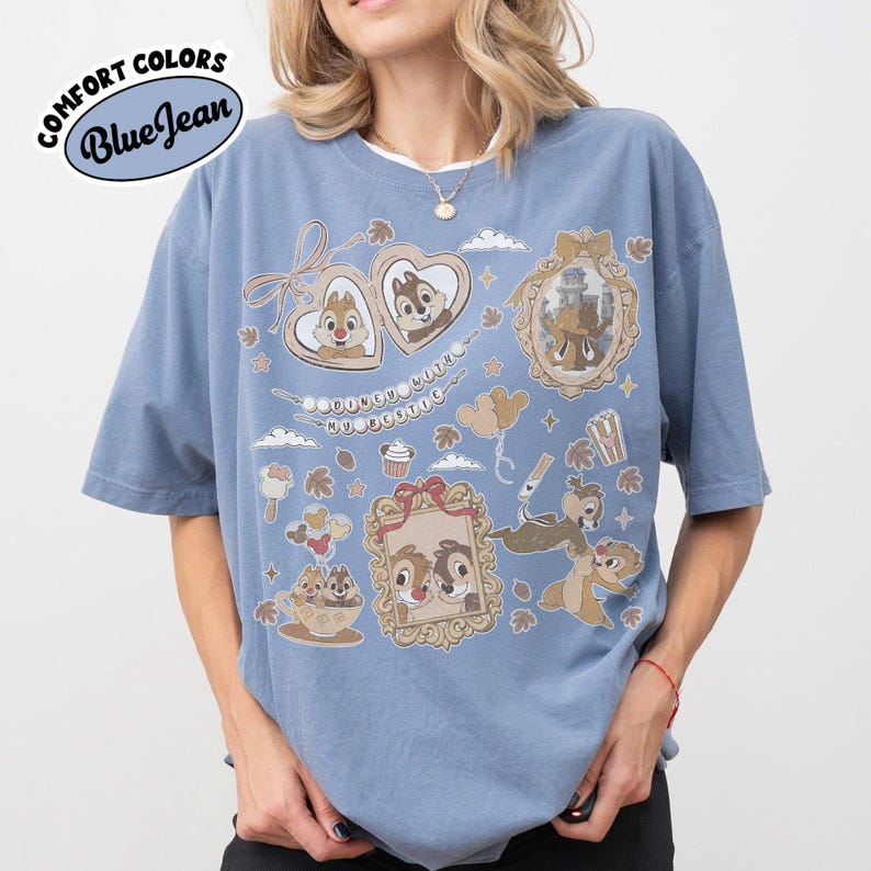 May include: Blue t-shirt with a graphic design featuring Chip and Dale characters. The design includes heart-shaped frames, balloons, and other cartoon elements. The shirt has the text "COMFORT COLORS Blue Jean" in a circular design.