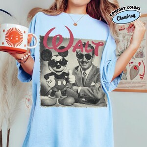K&ouml;nnte beinhalten: Hellblaues T-Shirt mit einem Vintage-Grafik von Mickey Mouse und Walt Disney, mit dem Wort "WALT" in Rot. Das Shirt hat eine lockere Passform und die Worte "COMFORT COLORS" und "Chambray" sind oben rechts aufgedruckt.