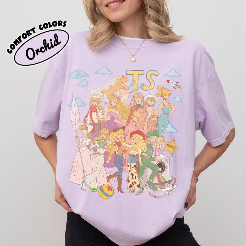 May include: A light purple short-sleeve t-shirt featuring a graphic print of various animated characters in diverse outfits, including a space suit, cowboy attire, and formal gowns. The text "TS" appears at the top, with clouds and a rocket.