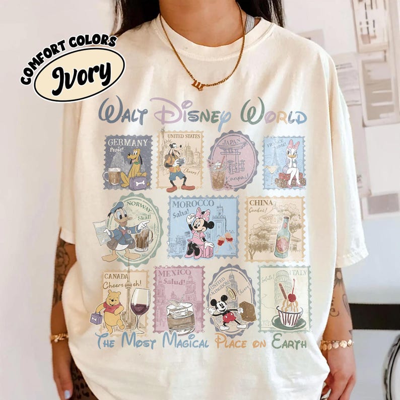 May include: Ivory-colored t-shirt featuring a colorful graphic of Disney characters and stamps representing various countries. The text "WALT DISNEY WORLD" and "THE MOST MAGICAL PLACE ON EARTH" are also displayed. The shirt has a relaxed fit.