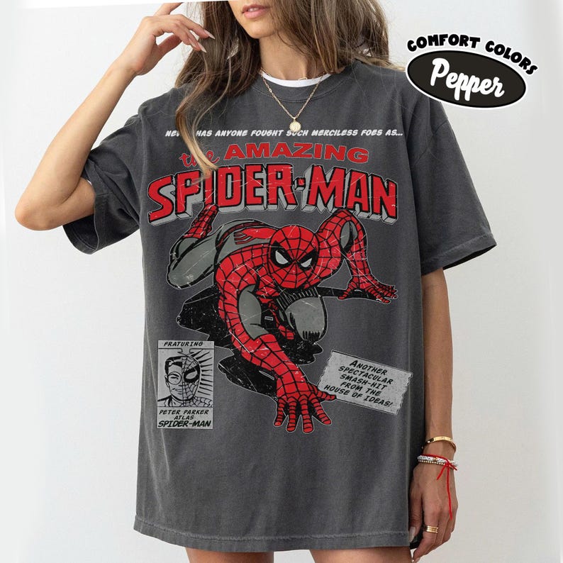 May include: A charcoal gray short-sleeve t-shirt featuring a vintage-style graphic of Spider-Man in red and black. The print includes the text The Amazing Spider-Man, Peter Parker, and Another Spectacular Smash-Hit From The House Of Ideas.