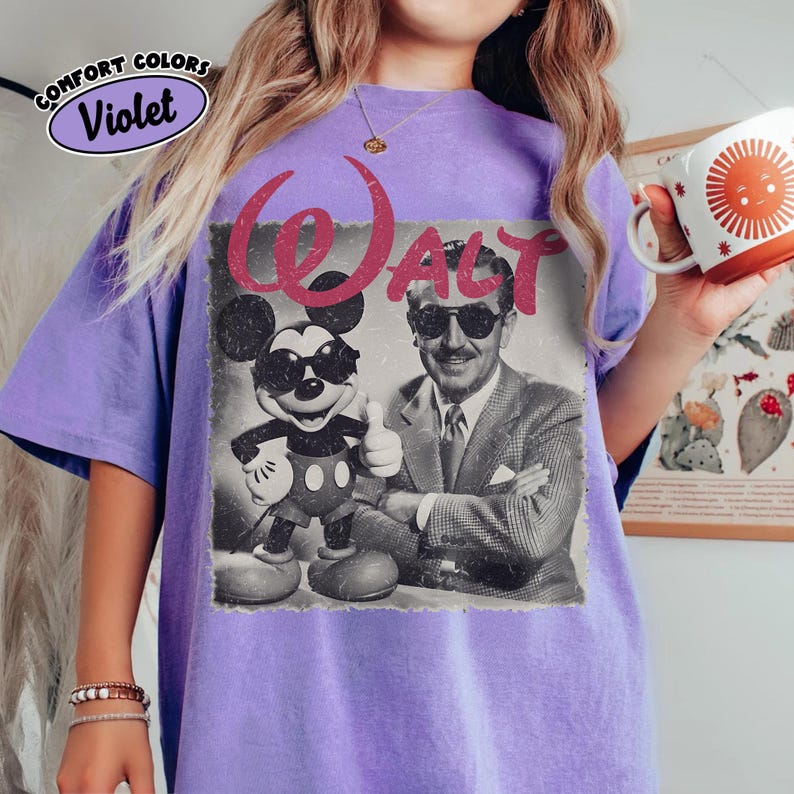 K&ouml;nnte beinhalten: Violettes Comfort Colors T-Shirt mit einem Vintage-Grafik von Mickey Mouse und Walt Disney. Die Grafik enth&auml;lt das Wort "WALT" in Rosa. Mickey Mouse tr&auml;gt eine Sonnenbrille und Walt Disney gibt einen Daumen hoch.