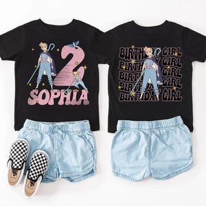 K&ouml;nnte beinhalten: Zwei schwarze T-Shirts mit Cartoon-Grafiken und Text, kombiniert mit hellblauen Jeansshorts und karierten Slip-On-Schuhen. Ein Shirt sagt "Sophia" und das andere sagt "Birthday Girl".