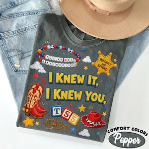 May include: A charcoal gray t-shirt featuring a graphic print with red cowboy boots, a red cowboy hat, a beaded bracelet with the text You've got a friend in me, a sheriff badge with Infinity and Beyond, and blocks with TS5, plus yellow stars.