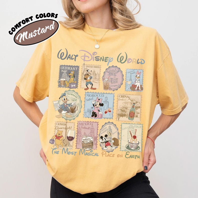 May include: Mustard-colored t-shirt featuring a Walt Disney World design. The shirt has a stamp-like graphic with Disney characters and country names. Text includes "The Most Magical Place on Earth."
