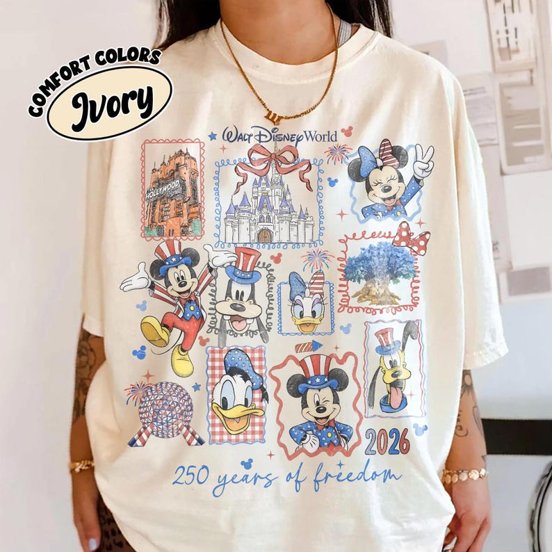 May include: Ivory-colored t-shirt with a Disney World design. The shirt features various Disney characters and landmarks in a stamp-like design, with the text "250 years of freedom" and "2026".