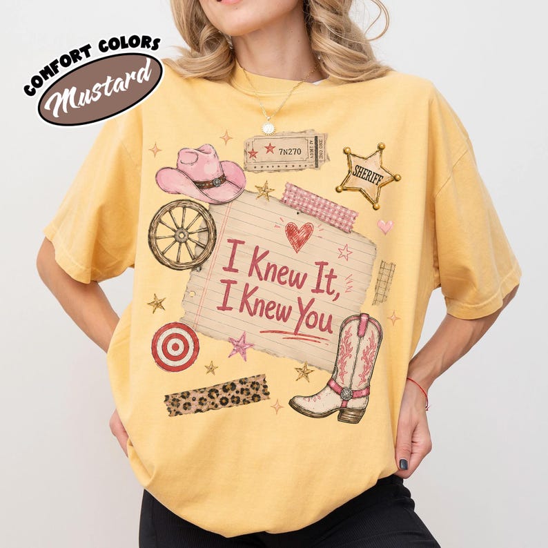 Puede incluir: Una camiseta de manga corta color amarillo mostaza con un estampado gr&aacute;fico de un sombrero de vaquero rosa, una rueda de carreta, una estrella de sheriff, un boleto y una bota. El centro muestra una nota con l&iacute;neas y el texto I Knew It, I Knew You.